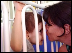 Young child in crib looking at his mom